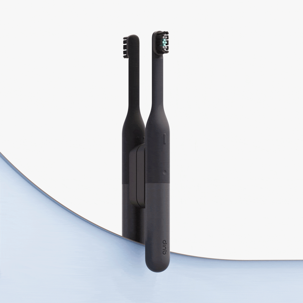 Wall-mounted black electric toothbrush attached to a mirror, with its reflection visible, set against a clean, minimal background with a curved blue accent.