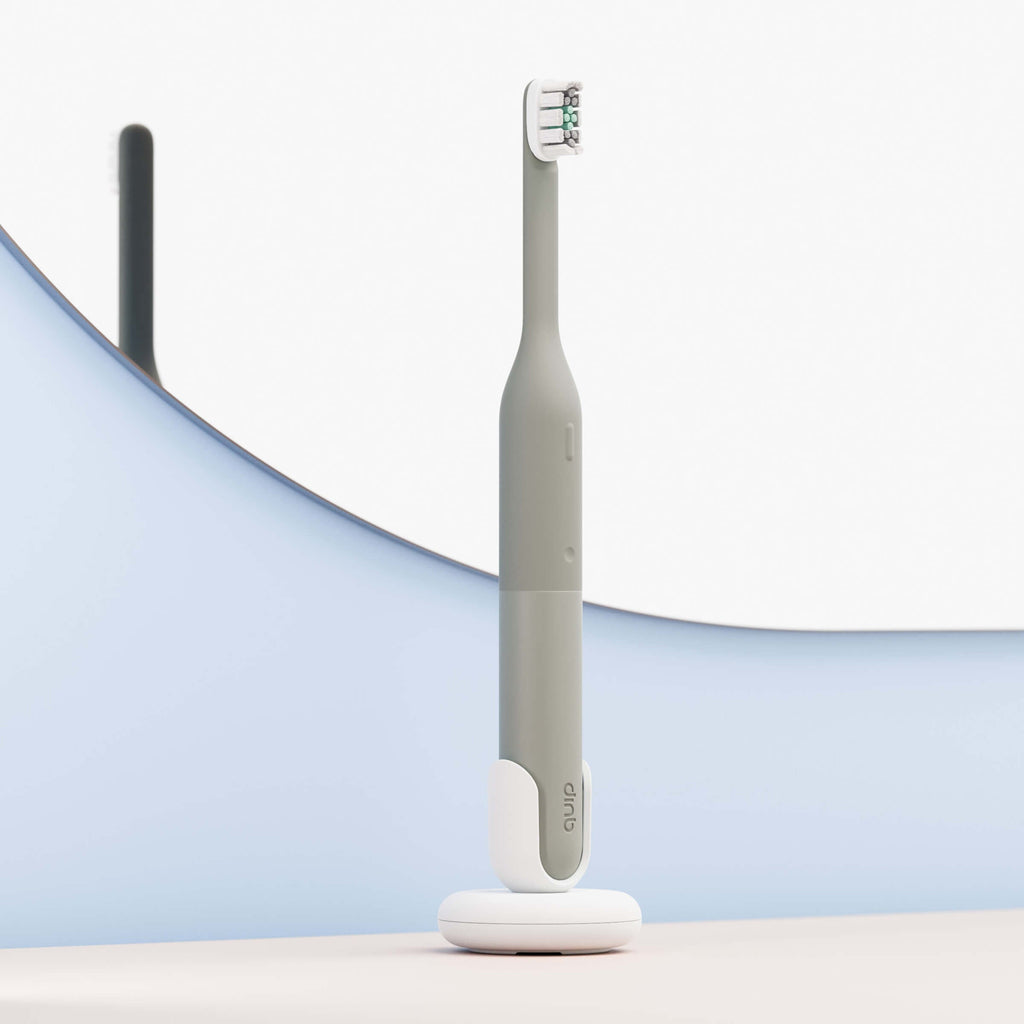 Gray electric toothbrush on a white stand with a blurred background